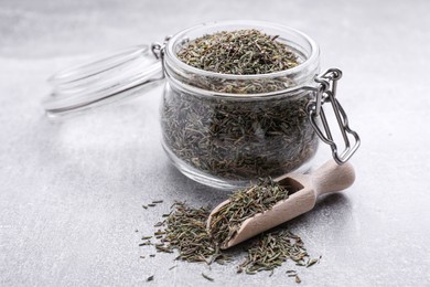 Jar and scoop with dried thyme on grey table, closeup
