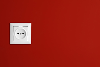 Image of Red wall with power socket, space for text. Electrical supply