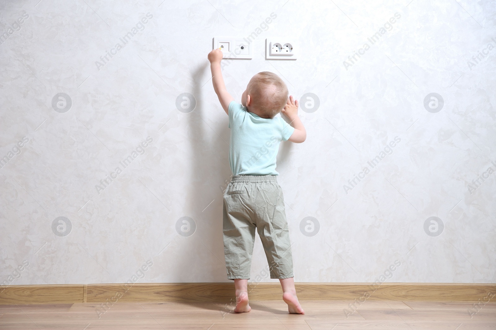 Photo of Little child playing with electrical socket indoors, back view. Dangerous situation