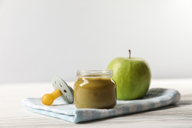 Photo of Jar with healthy baby food, apple and pacifier on white wooden table