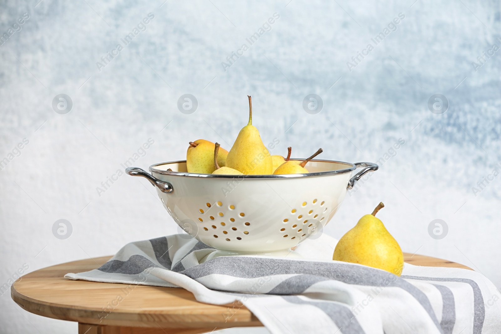 Photo of Colander with pears on table against color background