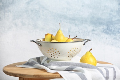 Photo of Colander with pears on table against color background