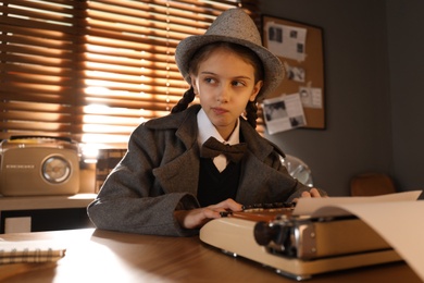 Photo of Cute little detective using typewriter at table in office