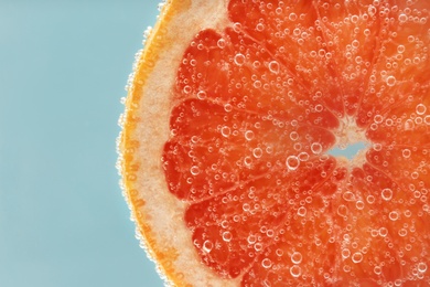 Photo of Slice of grapefruit in sparkling water on light blue background, closeup. Citrus soda