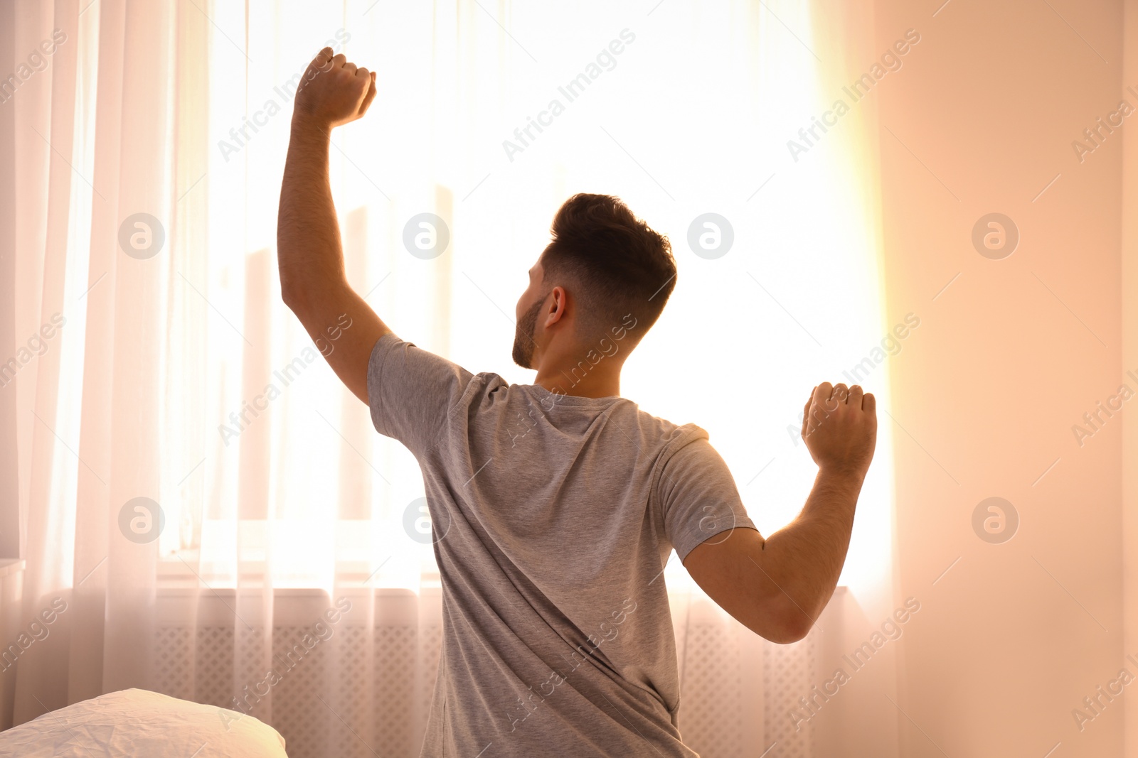 Photo of Young man stretching on bed at home, view from back. Lazy morning