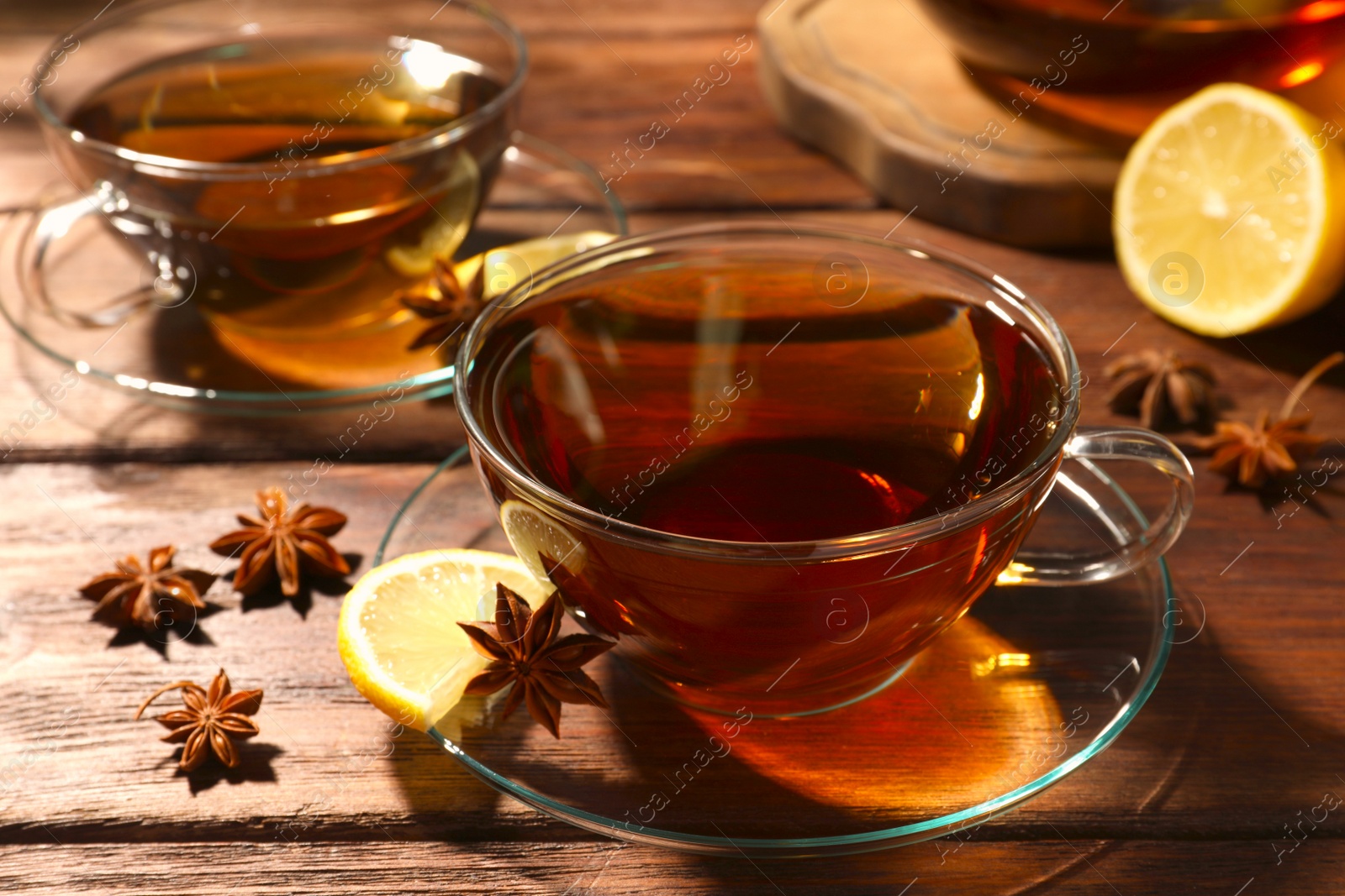 Photo of Aromatic tea with anise stars and lemon on wooden table, closeup