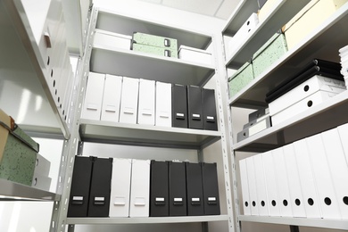Folders and boxes with documents on shelves in archive, low angle view