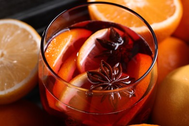 Photo of Glass of aromatic punch drink and fresh citrus fruits on table, closeup