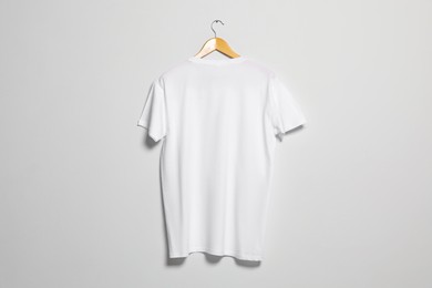 Photo of Hanger with white t-shirt on light wall. Mockup for design