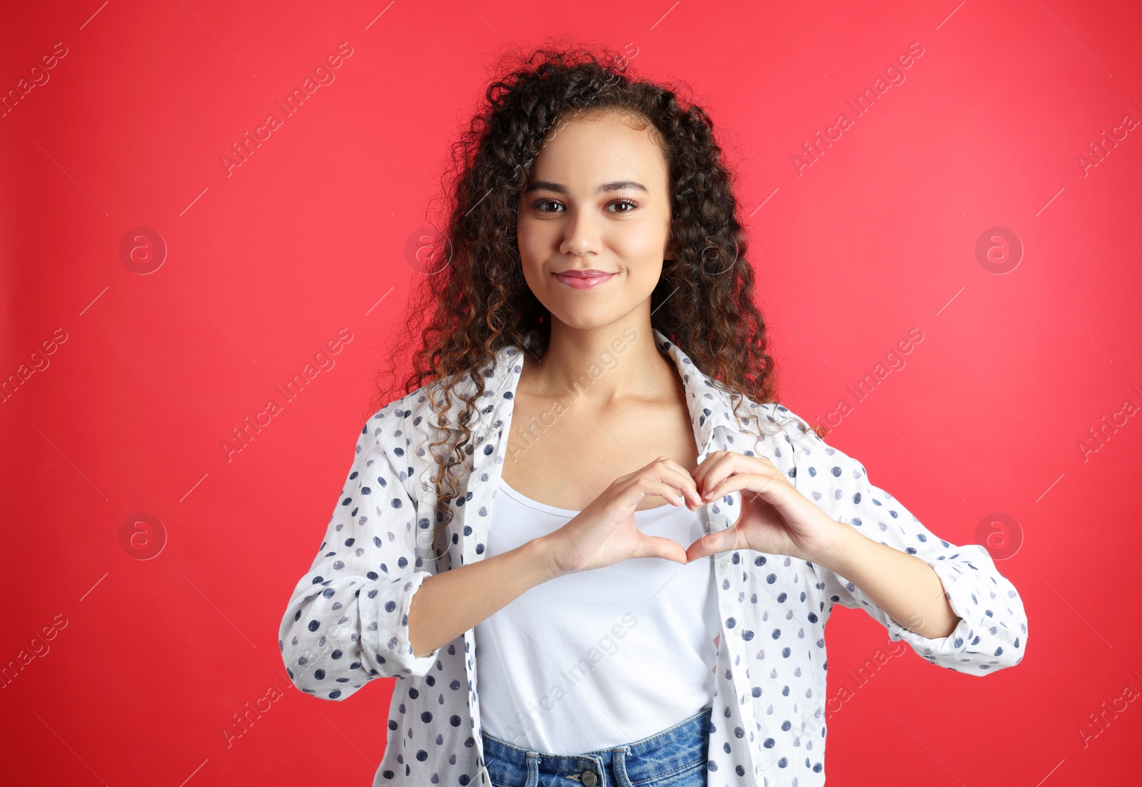 Photo of Happy young African-American woman making heart with hands on red background