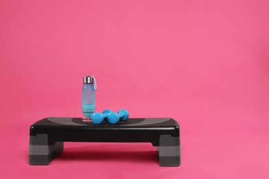 Photo of Step platform, dumbbells and bottle of water on pink background, space for text. Sports equipment