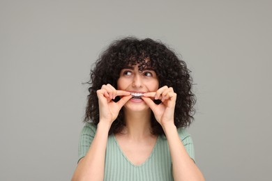 Photo of Young woman applying whitening strip on her teeth against grey background