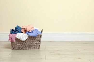 Photo of Wicker laundry basket full of dirty clothes on floor near color wall. Space for text