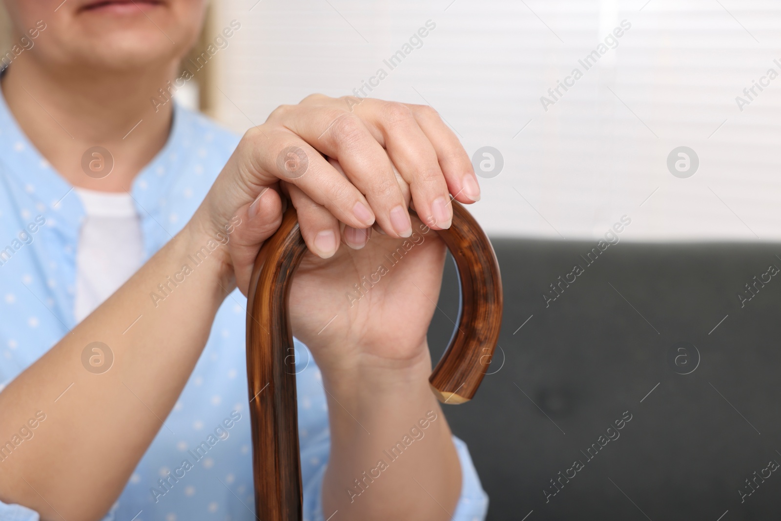 Photo of Senior woman with walking cane sitting on sofa at home, closeup. Space for text