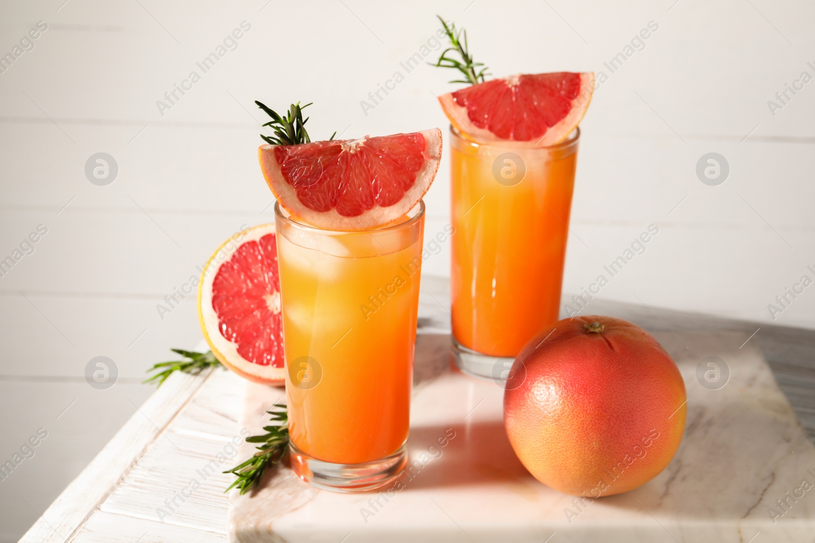 Photo of Tasty grapefruit drink with ice in glasses, rosemary and fresh fruits on light wooden table