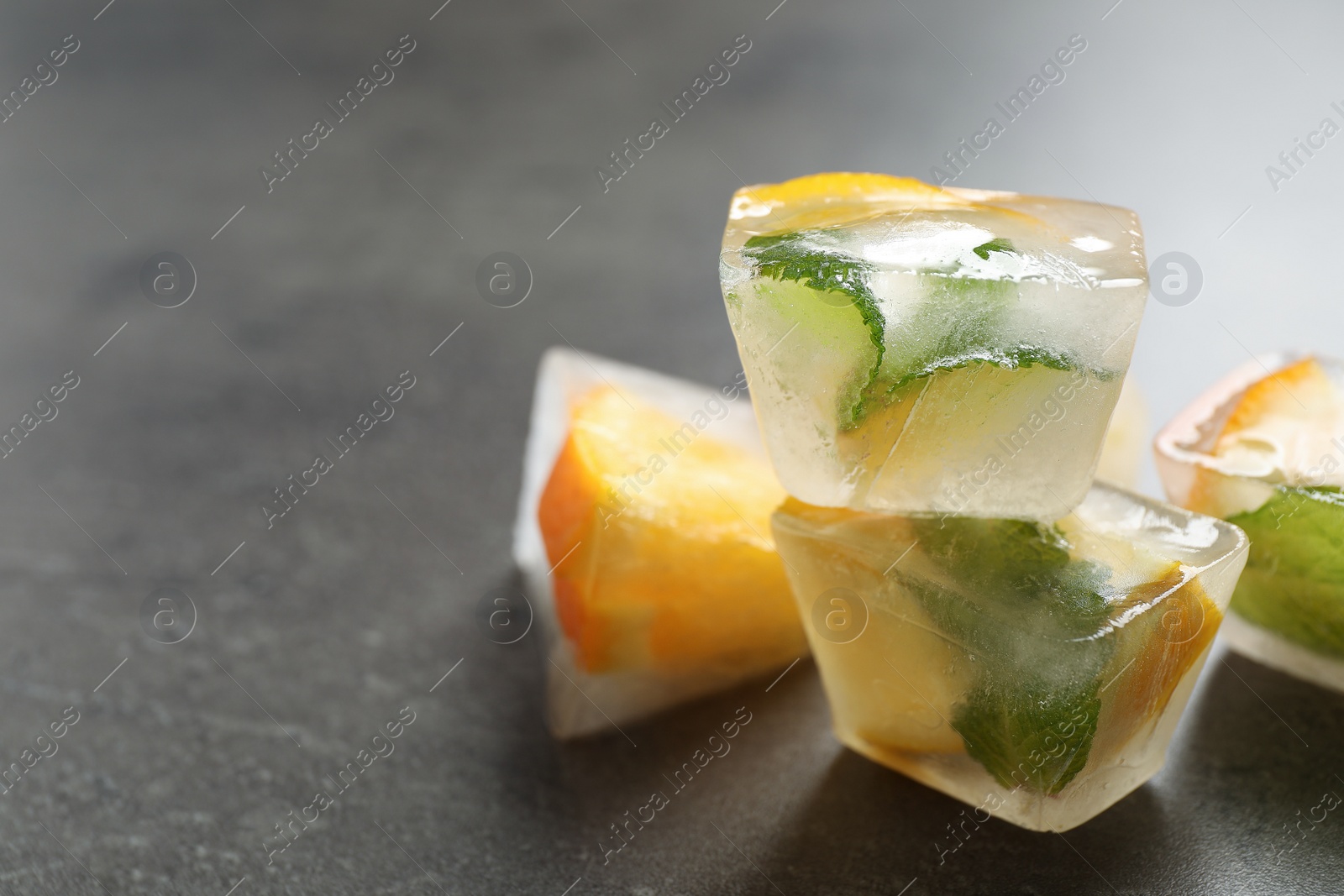 Photo of Ice cubes with orange and mint on grey table, closeup. Space for text