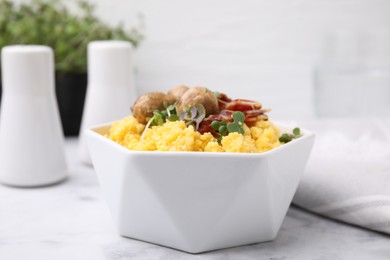 Photo of Cooked cornmeal with bacon, mushrooms and microgreens in bowl on white marble table, closeup