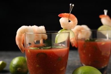 Tasty shrimp cocktail with sauce in glasses and limes on grey table against black background, closeup
