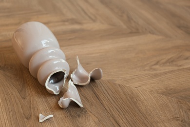 Photo of Broken pink ceramic vase on wooden floor. Space for text