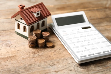 House model with coins and calculator on wooden table. Real estate agent service