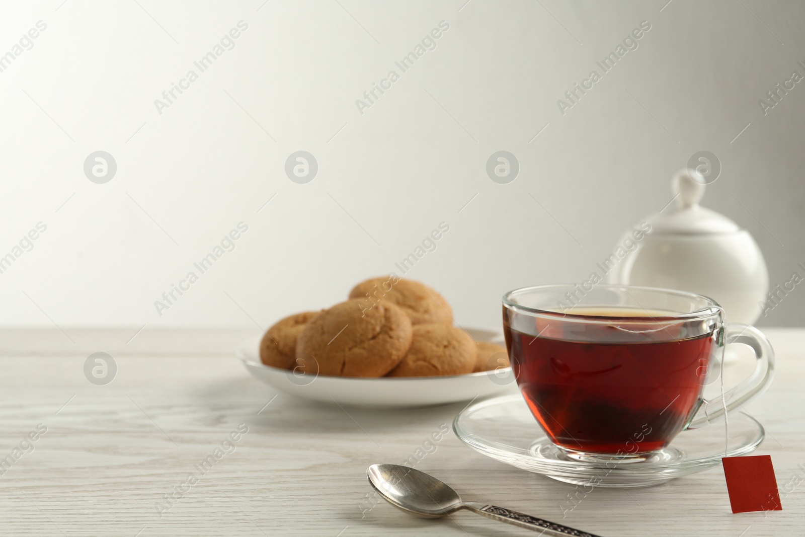 Photo of Tea bag in glass cup of hot water on white wooden table. Space for text