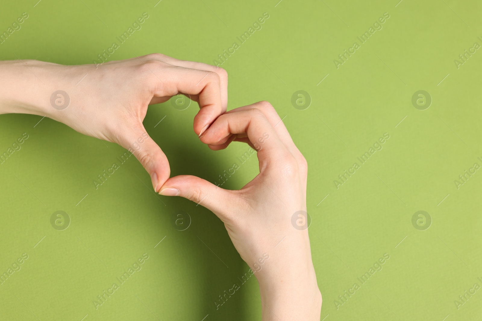 Photo of Woman showing heart gesture with hands on green background, top view. Space for text