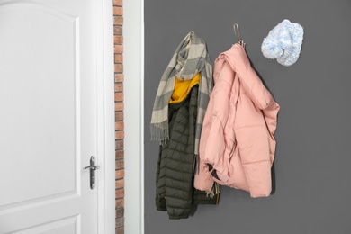 Photo of Different clothes hanging on grey wall near door. Hallway interior elements