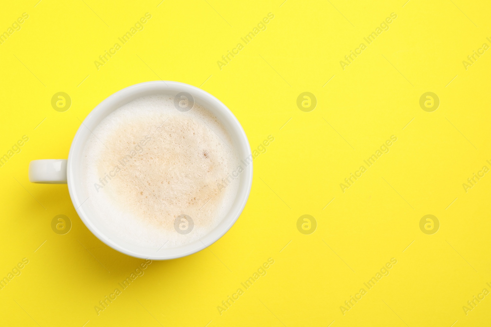 Photo of Aromatic coffee in cup on yellow background, top view. Space for text