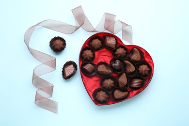 Heart shaped box with delicious chocolate candies and ribbon on light blue background, flat lay