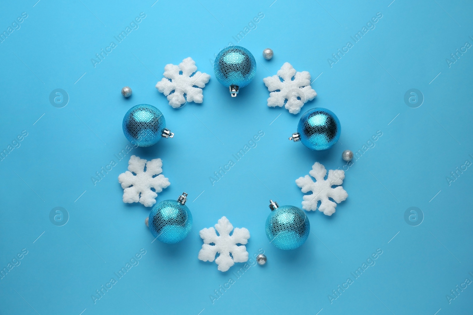 Photo of Bright festive wreath made of Christmas balls and decorative snowflakes on light blue background, top view. Space for text