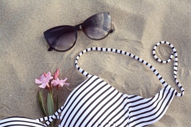 Photo of Beautiful sunglasses, swimsuit and tropical flower on sand