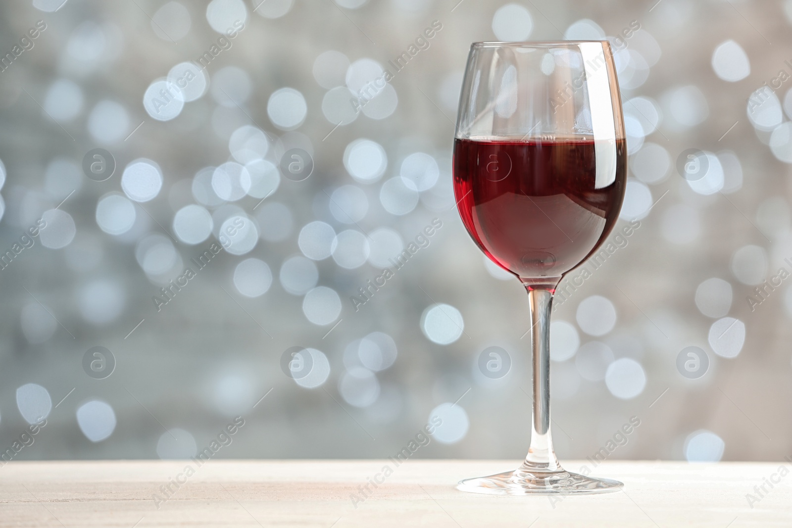 Photo of Glass of wine on table against blurred lights, space for text