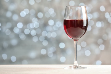 Photo of Glass of wine on table against blurred lights, space for text