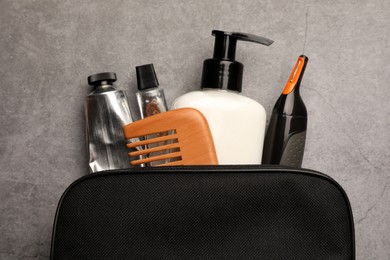 Photo of Preparation for spa. Compact toiletry bag with different cosmetic products on grey textured background, top view