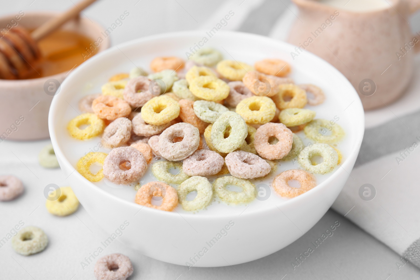 Photo of Cereal rings and milk in bowl on white table, closeup