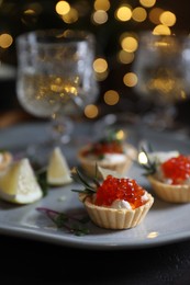 Delicious tartlets with red caviar, cream cheese and lemon served near wine on black table, closeup. Space for text