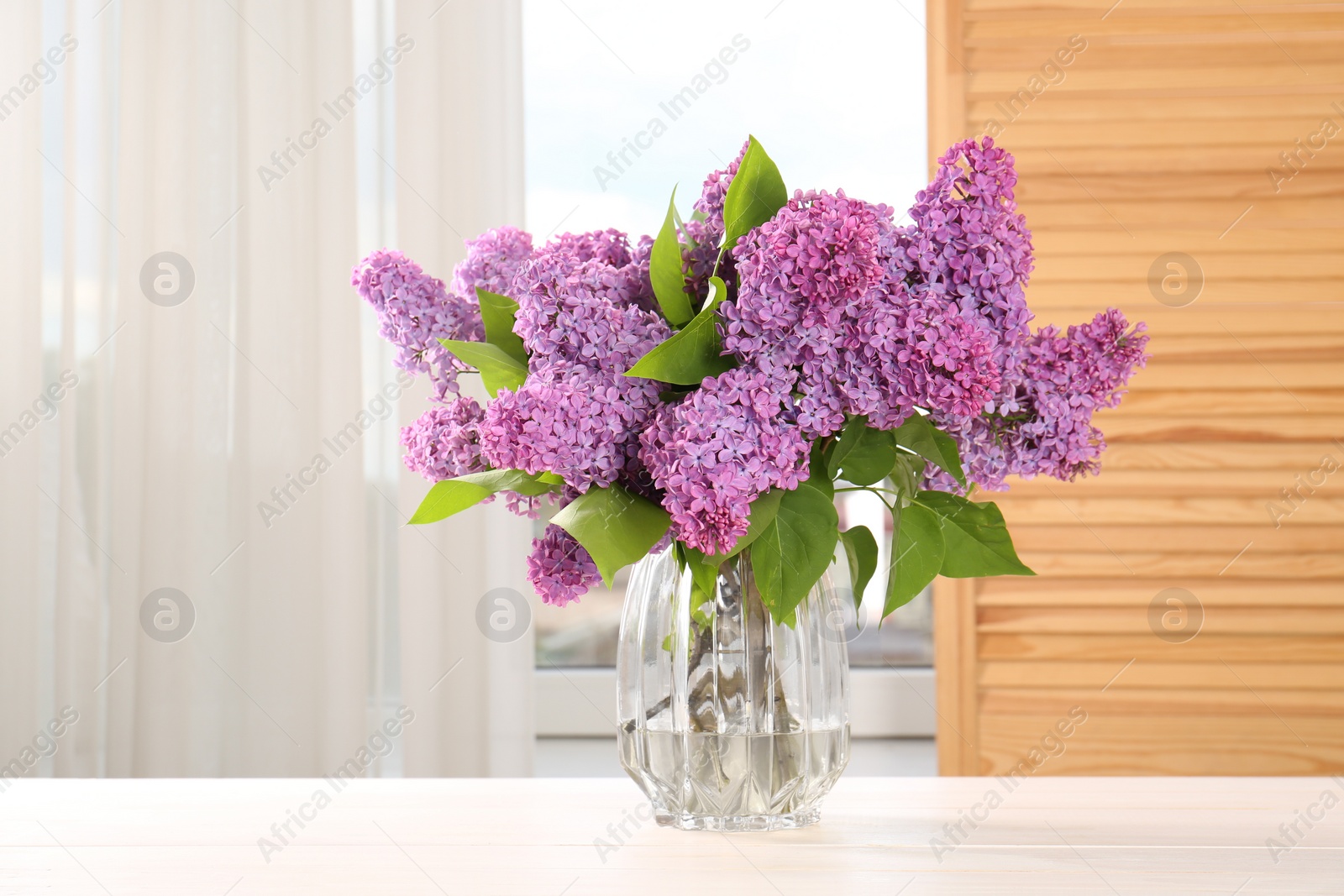 Photo of Beautiful lilac flowers in vase on white wooden table indoors