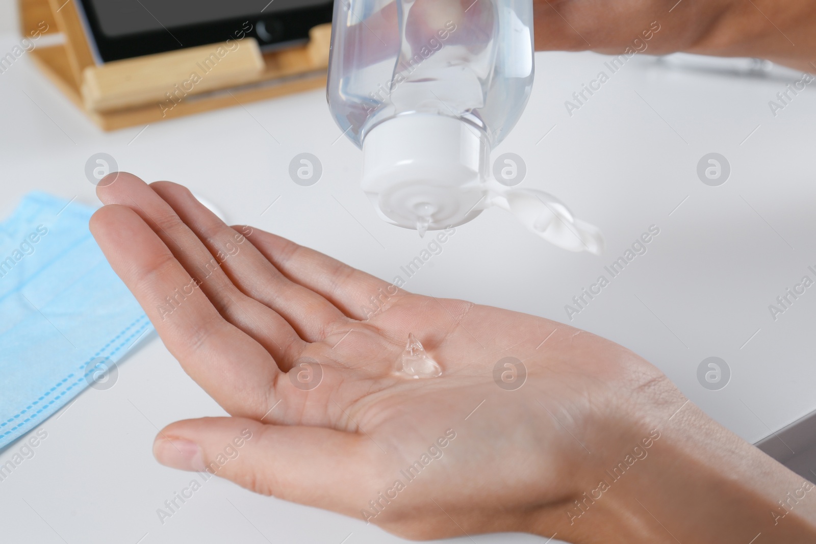 Photo of Woman applying hand sanitizer at white table, closeup. Personal hygiene during COVID-19 pandemic