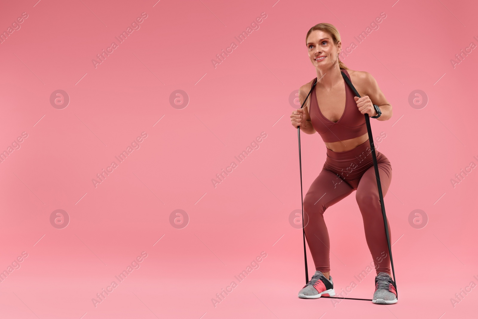 Photo of Woman exercising with elastic resistance band on pink background, low angle view. Space for text