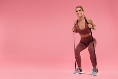 Woman exercising with elastic resistance band on pink background, low angle view. Space for text