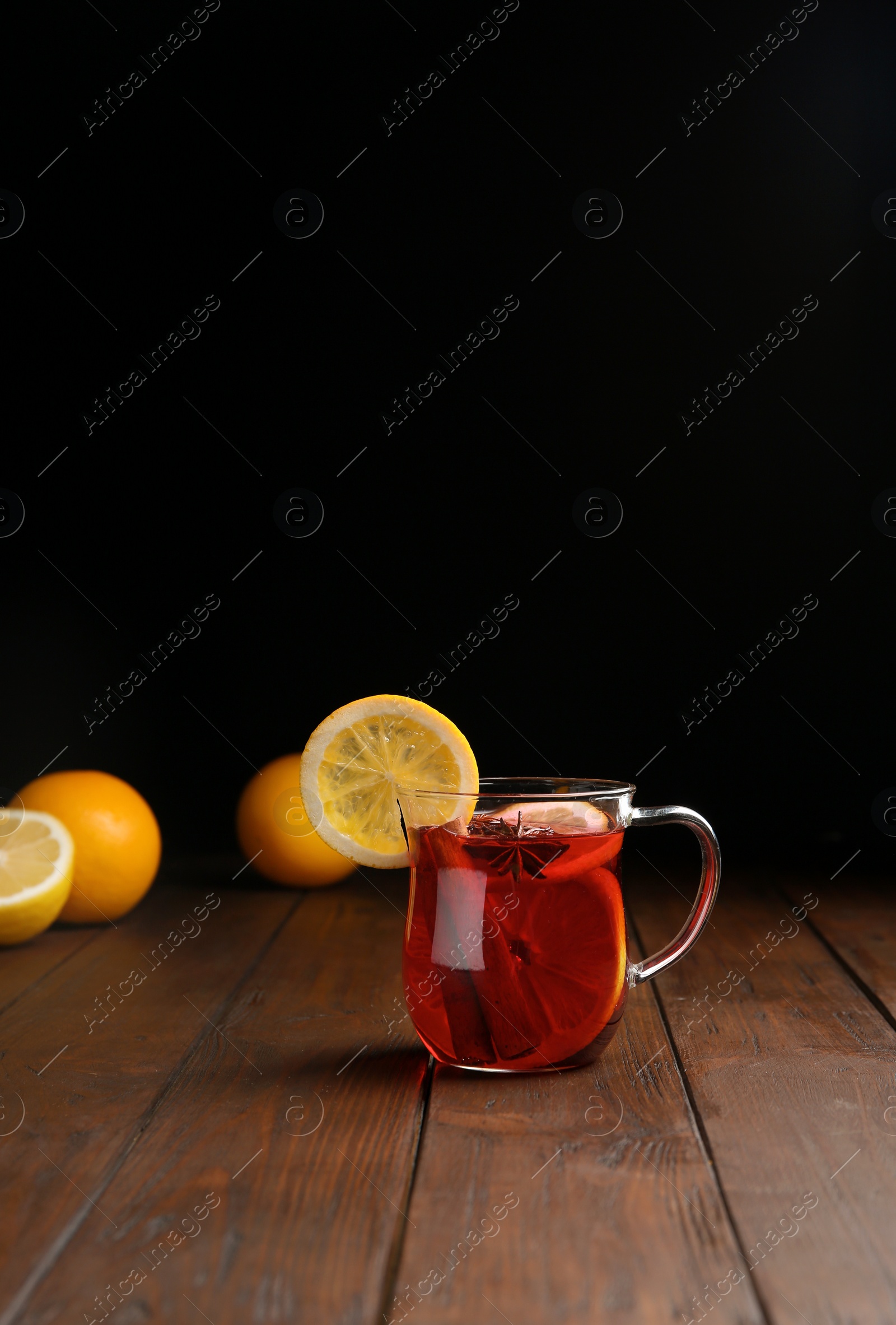 Photo of Cup with red mulled wine on wooden table against dark background. Space for text