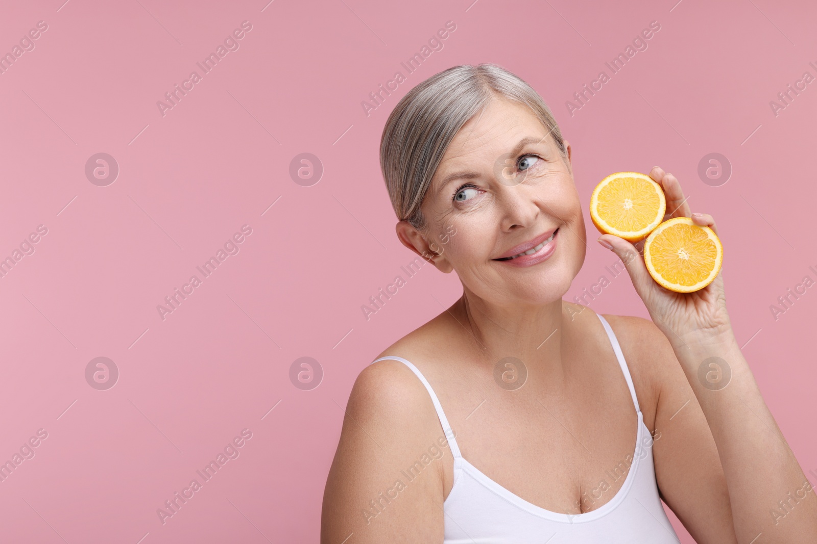 Photo of Beautiful woman with halves of orange rich in vitamin C on pink background, space for text