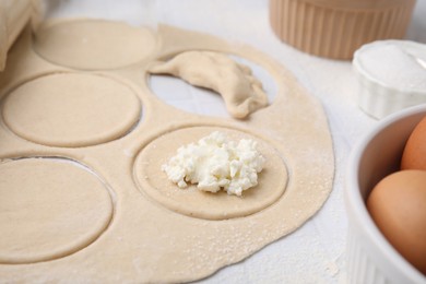 Photo of Process of making dumplings (varenyky) with cottage cheese. Raw dough and other ingredients on white tiled table, closeup