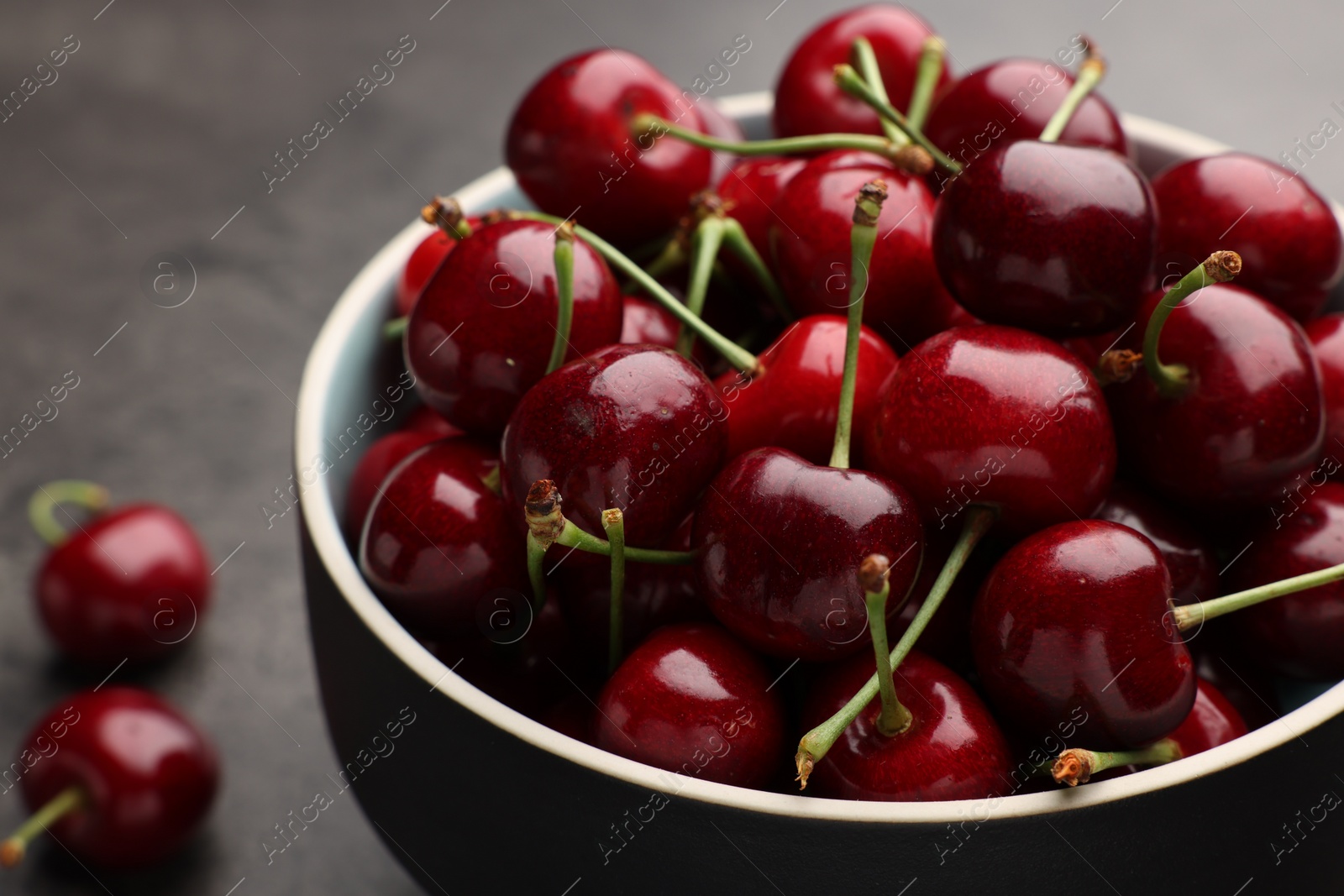 Photo of Bowl with ripe sweet cherries on grey table, closeup