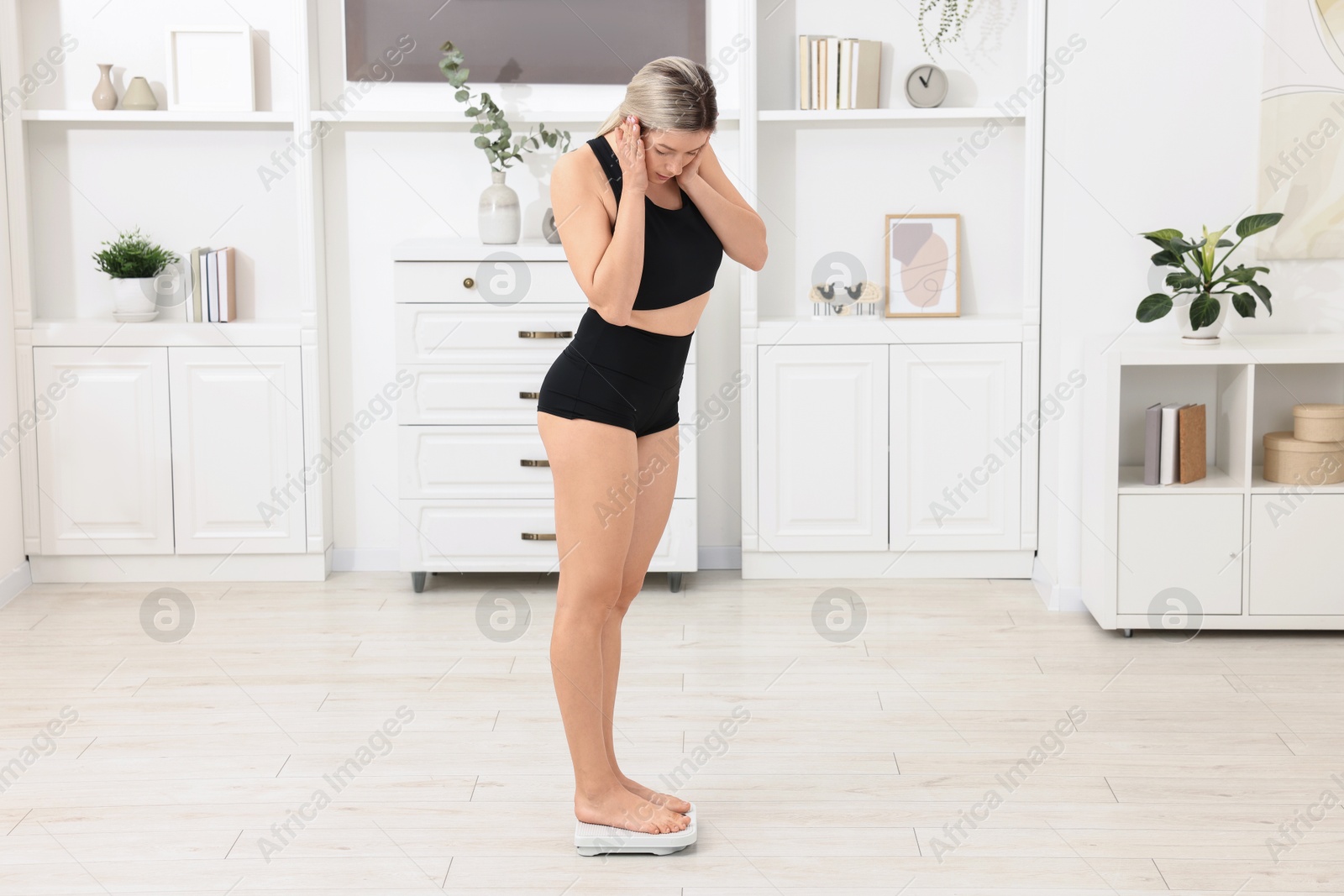 Photo of Surprised woman standing on floor scales at home