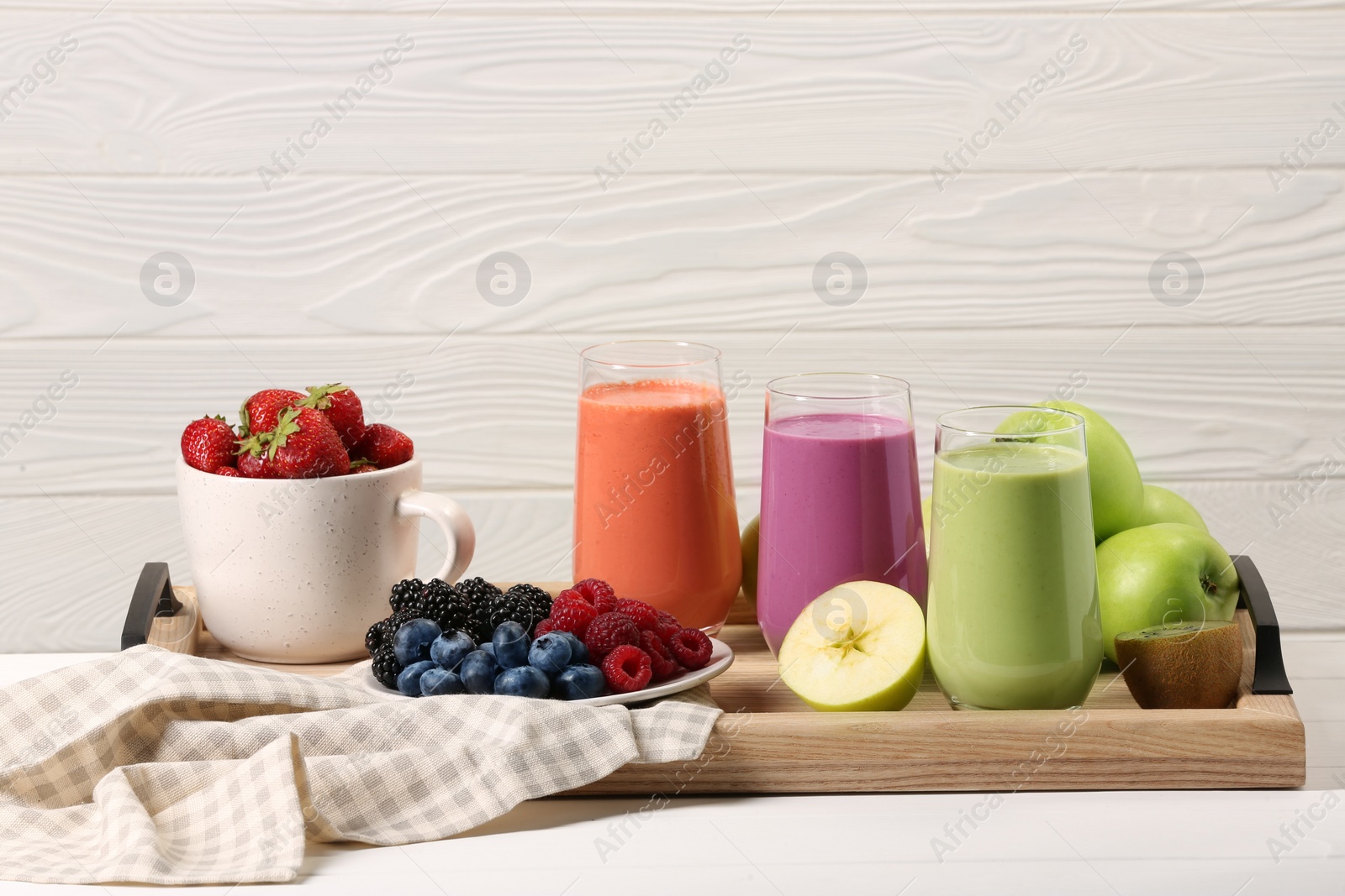 Photo of Glasses of different tasty smoothies and fresh ingredients on white wooden table