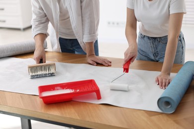 Woman and man applying glue onto wallpaper sheet at wooden table indoors, closeup