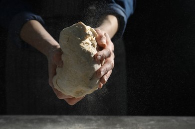 Photo of Making bread. Woman kneading dough at table on dark background, closeup. Space for text