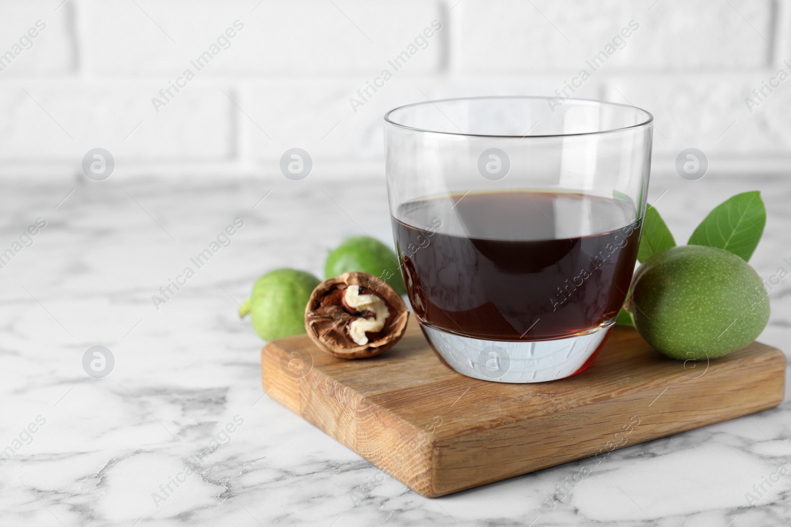 Photo of Delicious liqueur and fresh walnuts on white marble table, space for text