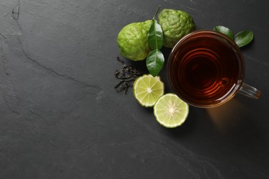 Glass cup of tasty bergamot tea, dry leaves and fresh fruits on black table, flat lay. Space for text